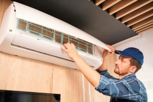 Young household technician opening lid of air conditioner to check what is wrong with it while doing his work